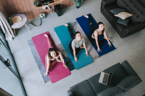 a group of asian chinese female friends practicing yoga in domestic living room together using laptop for online class  asian yoga pants stock pictures, royalty-free photos & images