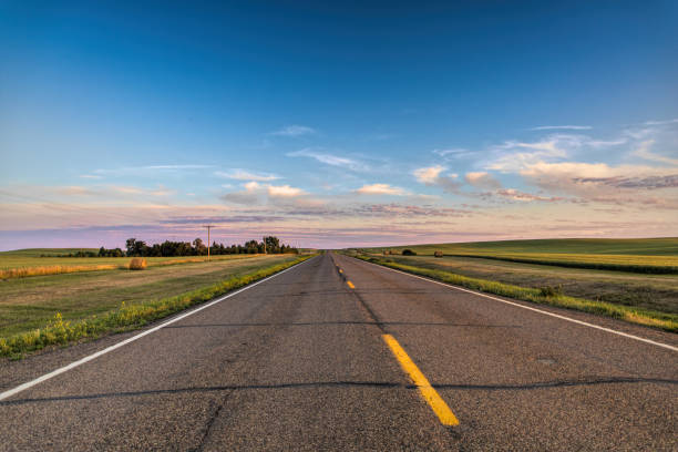 a long country highway rural highway road in North Dakota at sunset with a colorful sky a long country highway rural highway road in North Dakota at sunset with a colorful sky north dakota stock pictures, royalty-free photos & images