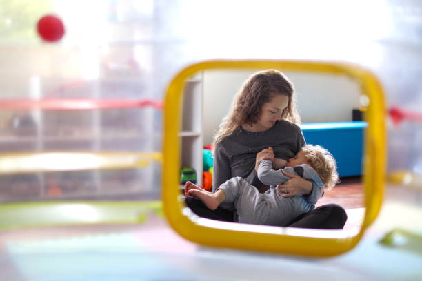 een moeder borst voedt haar peuter in de speelkamer thuis. - borstvoeding stockfoto's en -beelden