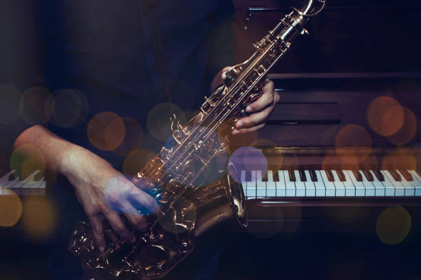 a musician plays alto saxophone over the piano stock photo