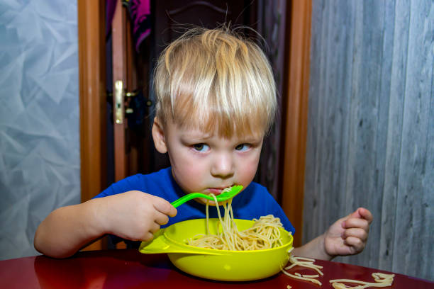 un petit enfant mange des nouilles dans la cuisine, - note gourmande photos et images de collection