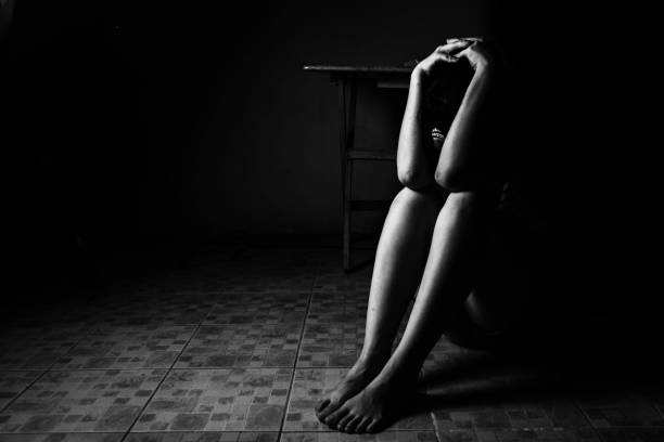 una mujer sentada en el suelo con el brazo en la parte baja la cabeza, la violencia sexual, abuso sexual, concepto de tráfico humano - foto de stock