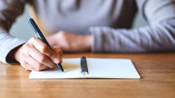 テーブルの上に白紙のノートに書いている女性 ストックフォト