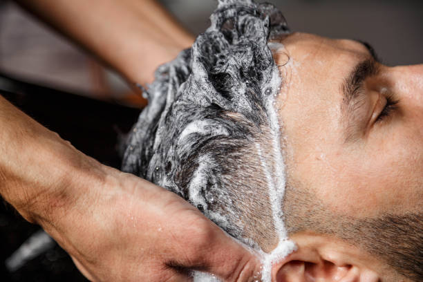 a young dark-haired guy of Indian or Asian appearance in a Barber shop on a black chair. the Barber washes his head with shampoo. stock photo