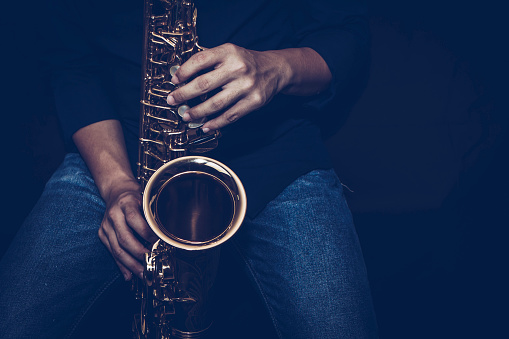 Close up of a young musician man hands hold and playing saxophone on black background with copy space. Can be used for music poster background