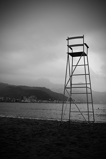 A misty day in october. The beach in Giardini Naxos at end of summer season. An empty life guard highchair overlooks the empty bay.