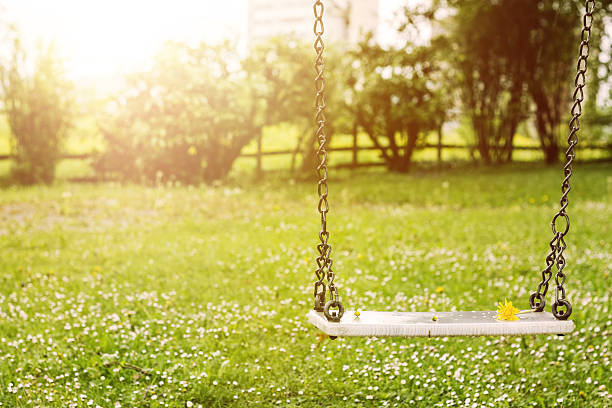 Abandoned swing in warm sunny light with flowers in the spring season