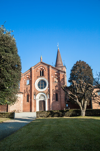 Church of Viboldone, with bell tower, arches, statues and trees during a sunny day in the countryside of Milan.
