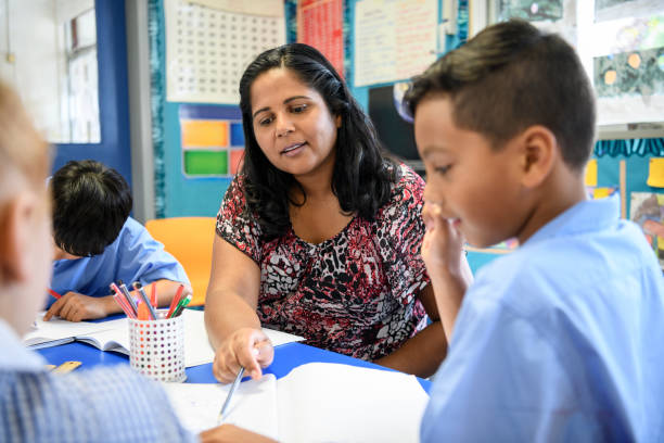 Aboriginal primary school teacher helping young boy in the classroom Australian female primary school teacher working with children offering support and guidance australian culture stock pictures, royalty-free photos & images
