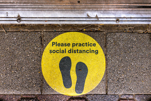 Above view for yellow warning sign to maintain social distance distancing during covid-19 coronavirus outbreak with footsteps on street Above view for yellow warning sign to maintain social distance distancing during covid-19 coronavirus outbreak with footsteps on street waiting in line photos stock pictures, royalty-free photos & images