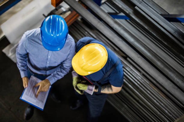 Above view of manager and manual worker reading reports in steel mill. High angle view of an inspector and steel worker going through reports in aluminum mill. steel mill stock pictures, royalty-free photos & images