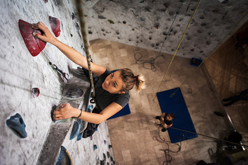 High angle view of an athletic woman exercising wall climbing with an assistance of male instructor.
