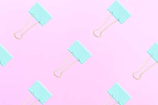 Abstract background. Pattern made of turquoise clips for papers on a pink background. Flat lay style. Background for business and education. Top view.