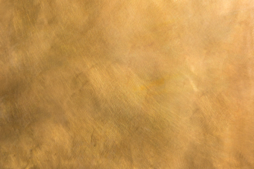 Brushed brown-golden copper or bronze surface, with visible brush strokes. The sheet metal has an appealing cloudy, wavy texture. Horizontal orientation. The image has been shot outdoors during natural day light, full frame and close up. Ideal for backgrounds. The dimensions of the photo are 5040 x 3360 px. High resolution.