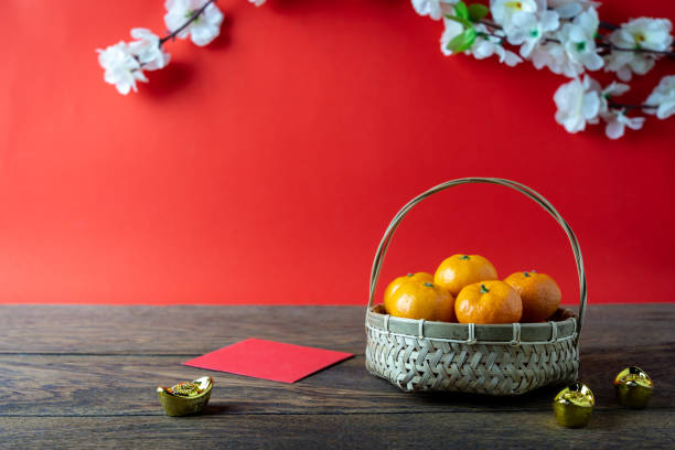 Accessories on Lunar New Year & Chinese New Year vacation concept background.Orange in wood basket with  red pocket money and flower on modern rustic brown & red backdrop at home office desk studio. stock photo