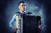 Musician playing the accordion against a black background. Fog in the background. Studio shot