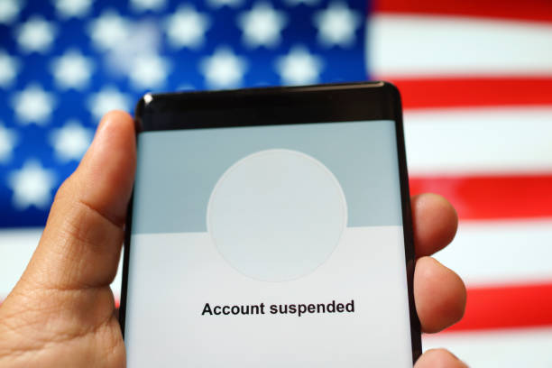 Account Suspended from a social media application against the American flag background Close up an adult hand holding a smartphone showing "Account Suspended" from a social media application against the American flag background. censorship stock pictures, royalty-free photos & images