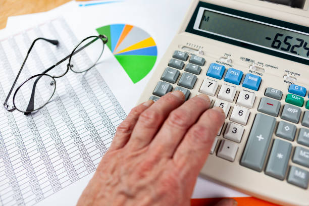 Accountant at his desk checking a spread sheet with a calculator Accountant at his desk checking a spread sheet printout with a calculator company liquidation stock pictures, royalty-free photos & images