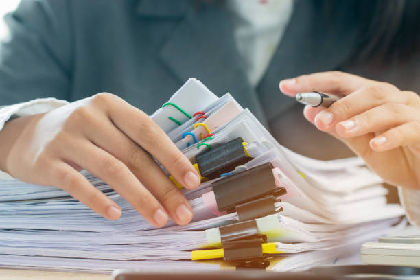Accounting planning budget concept : Business woman offices working for arranging documents unfinished stack of document papers with pen, calculator, clip papers on busy office desk stock photo