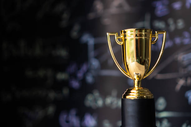 Achievement success in education awards concept: Golden trophy cup winner on blur formula equation blackboard background. Congratulation in university. stock photo