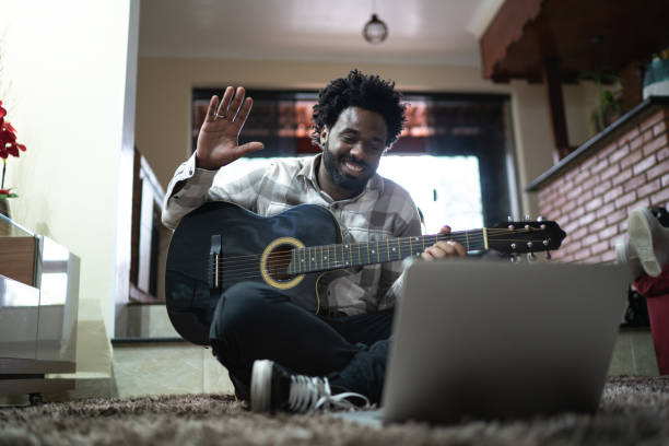 akustische gitarrenunterricht durch einen videoanruf, winkend zum laptop zu hause - musiker stock-fotos und bilder
