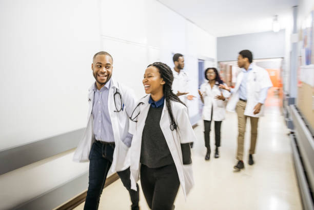 Action candid portrait of medical team walking down hospital corridor Blurred motion of busy medical students, nurses and doctors in hospital, on the move, wearing uniform, talking, smiling and laughing medical student stock pictures, royalty-free photos & images