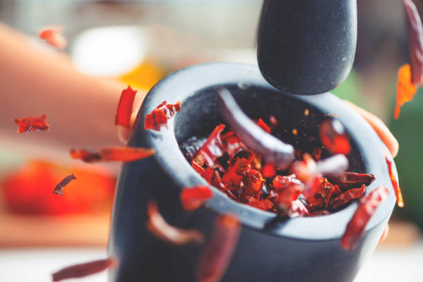 Action image of dried chilli peppers being crushed in a mortar and pestle. Action image of dried chilli peppers being crushed in a mortar and pestle. The chillis are flying out of the bowl as they are being smashed. Chillis are mostly whole. cayenne pepper stock pictures, royalty-free photos & images