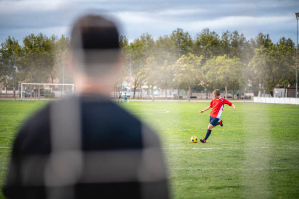 Action Portrait of Teenage Male Footballer Kicking to Goal Over the shoulder perspective through netting of foreground coach ready for kick to goal by 14 year old male athlete during training practice. custom spain soccer jerseys stock pictures, royalty-free photos & images