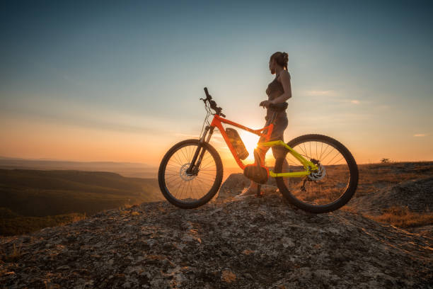 Active life A woman with a bike enjoys the view of sunset over an autumn forest electric bicycle stock pictures, royalty-free photos & images