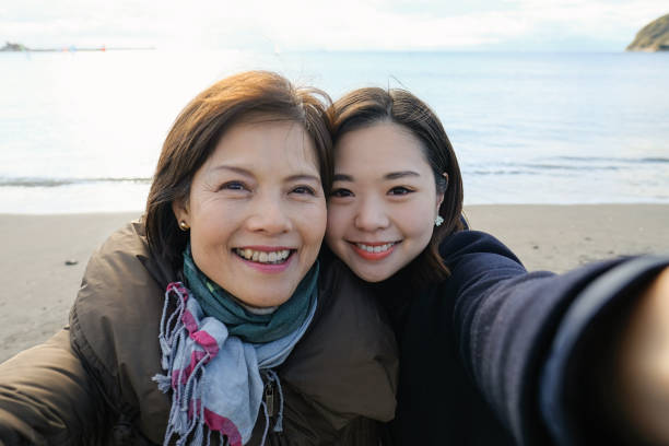 アクティブな成熟した女性と彼女の娘は、ビーチで自分撮りを取ります - 自撮り ストックフォトと画像