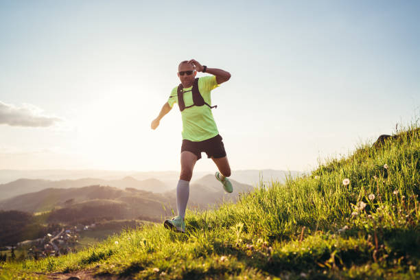 Active mountain trail runner dressed bright t-shirt with a backpack in sports sunglasses running endurance ultramarathon race by picturesque hills at sunset time. Sporty active people concept image. stock photo