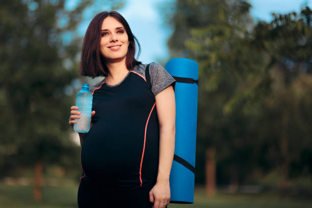 Active Pregnant Woman Holding Water Bottle Carrying a Yoga Mat stock photo
