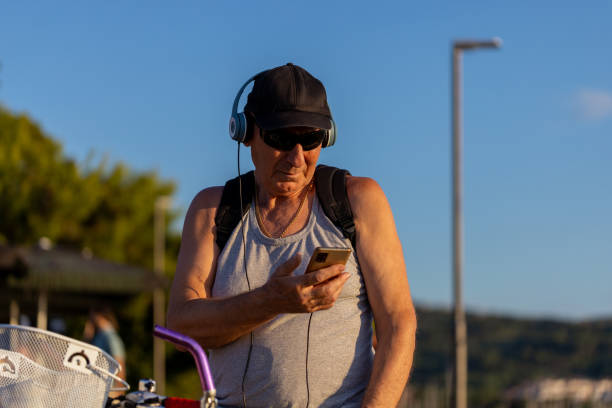 active senior gentleman with cap and sunglasses looking at phone - senior listening music beach bildbanksfoton och bilder