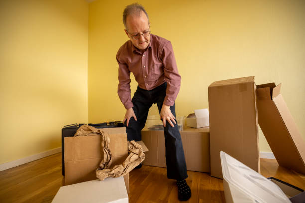 Active senior man alone in empty apartment room while moving house unpacking from cardboard boxes stock photo