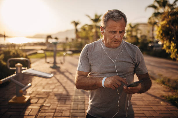 active senior man using smart phone - senior listening music beach bildbanksfoton och bilder