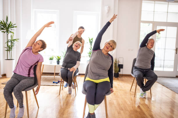 Active senior people practicing yoga during yoga class on chairs stock photo