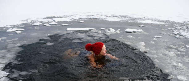 active senior woman swimming in water hole in frozen lake outdoors in winter, cold therapy concept. - ice swimming stockfoto's en -beelden
