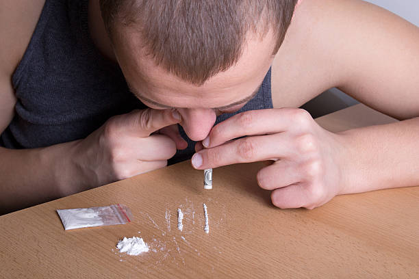 addicted man snorting heroin from the table addicted young man snorting heroin from the table snorting stock pictures, royalty-free photos & images