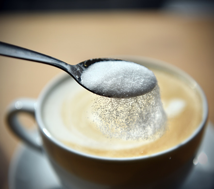 Sprinkling refined sugar from a spoon into a cup of coffee