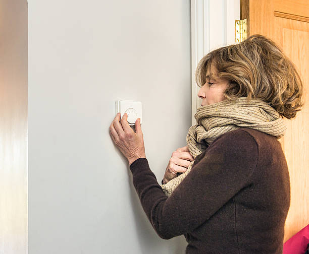 Adjusting the heating thermostat A woman dressed in a warm wool jumper and scarf, adjusting a home thermostat dial. thermostat stock pictures, royalty-free photos & images