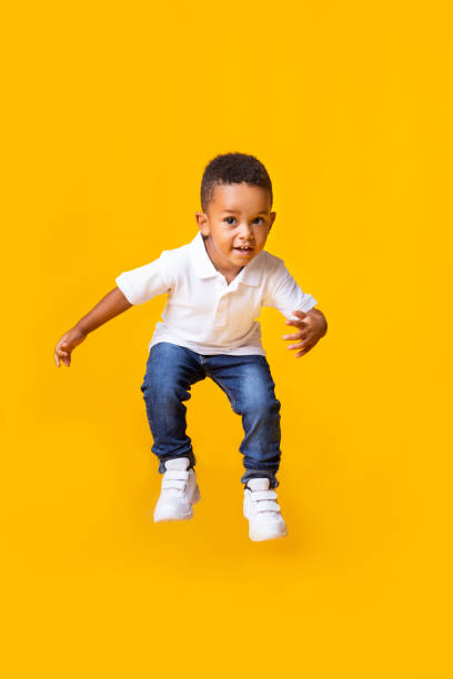 Adorable afro baby boy jumping over yellow studio background Adorable afro baby boy jumping over yellow studio background with copy space boy jumping stock pictures, royalty-free photos & images