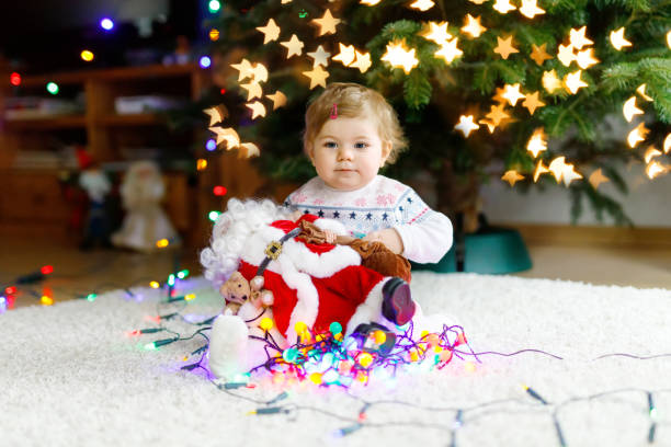 очаровательная девочка, держащая красочные гирлянды огней в милых руках. маленький ребенок в праздничной одежде украшает елку с семьей. пе� - weihnachten стоковые фото и изображения
