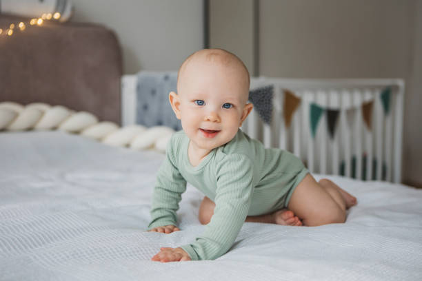 Adorable barefoot child smiling while sitting on bed stock photo