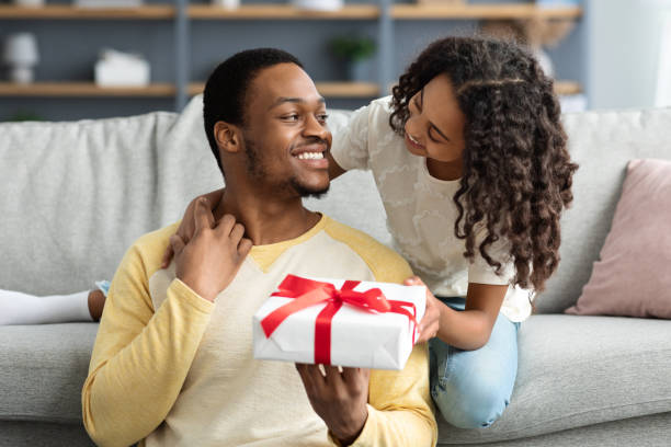 Adorable black girl greeting her smiling father Adorable black girl greeting her smiling young father, hugging him and giving gift box, living room interior, copy space. Happy african american daddy and daughter celebrating Fathers day at home fathers day stock pictures, royalty-free photos & images