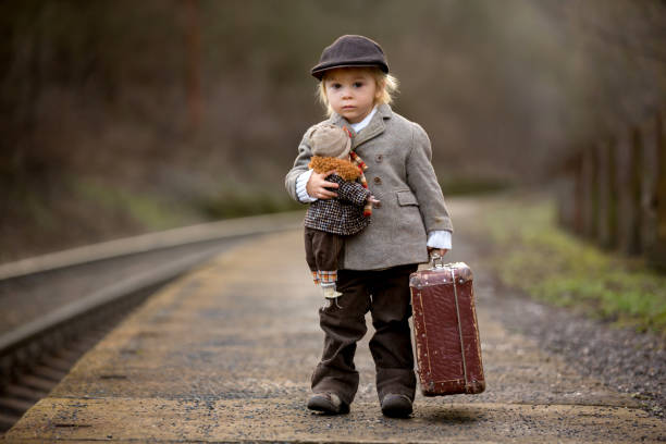 bir tren istasyonunda sevimli çocuk, bavul ve güzel vintage bebek ile tren bekliyor - teddy ray stok fotoğraflar ve resimler