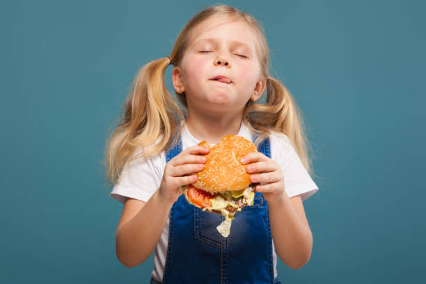 adorable petite fille mignonne en combinaison blanche de chemise et jean avec hamburger - eating burger photos et images de collection
