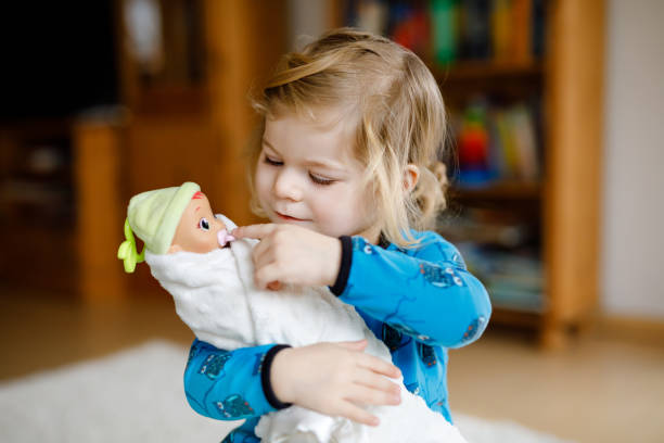 Adorable cute little toddler girl playing with doll. Happy healthy baby child having fun with role game, playing mother at home or nursery. Active daughter with toy. Adorable cute little toddler girl playing with doll. Happy healthy baby child having fun with role game, playing mother at home or nursery. Active daughter with toy doll stock pictures, royalty-free photos & images
