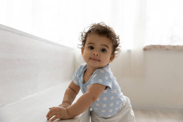 Adorable little african baby relying on furniture, making first steps. Portrait of adorable little african american baby boy or girl relying on furniture, learning making first steps indoors. Happy curious cute mixed race toddler walking, childcare development concept. babies only stock pictures, royalty-free photos & images