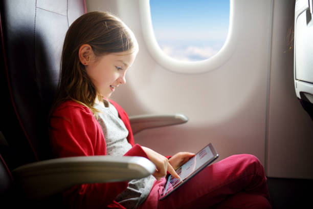 Adorable little girl traveling by an airplane. Child sitting by aircraft window and using a digital tablet stock photo