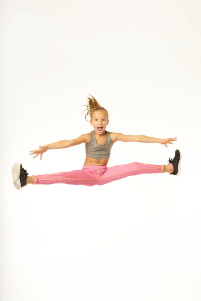 Adorable sporty girl jumping and doing splits in the air Cute female girl spreading hands to sides and screaming while making jump and performing gymnastic trick. Isolated on white background doing the splits stock pictures, royalty-free photos & images